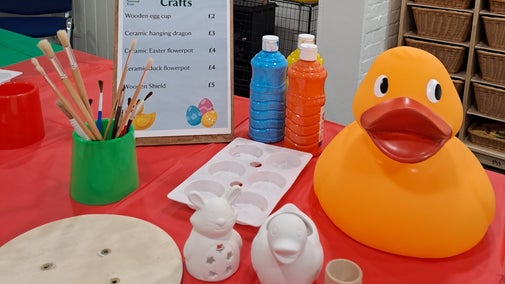 A table laid out with paint, paint brushes, wooden shields and ceramic animals to paint.